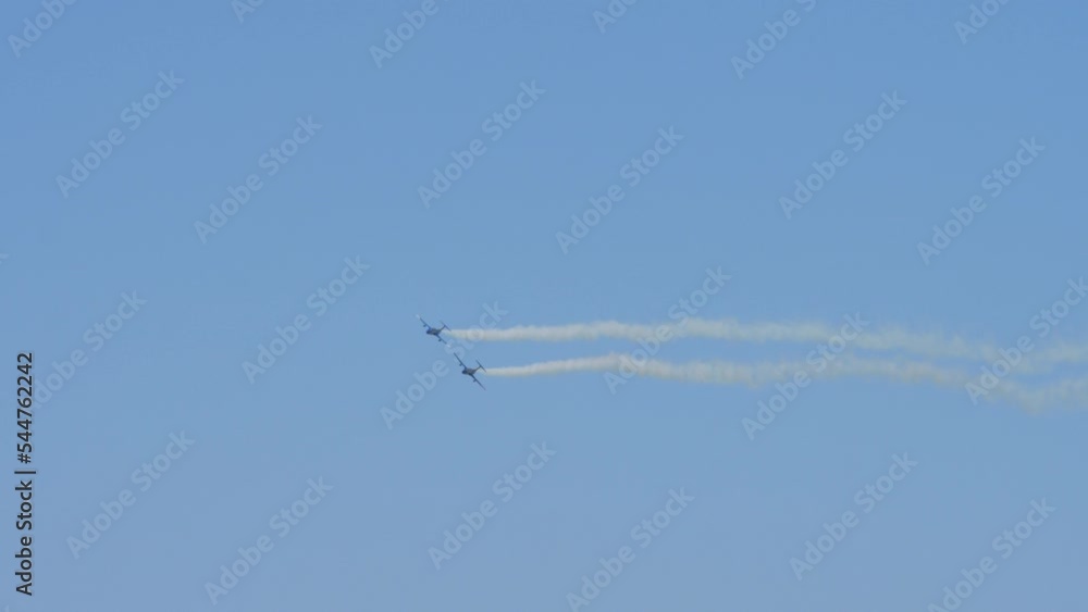 Two airplanes flying and perform aerobatics and flying maneuvers. White smoke trail left by aircrafts. Training, recreation, entertainment, sport concept. Clear blu sky background, no clouds Two airplanes flying and perform aerobatics and flying maneuvers. White smoke trail left by aircrafts. Training, recreation, entertainment, sport concept. Clear blu sky background, no clouds
