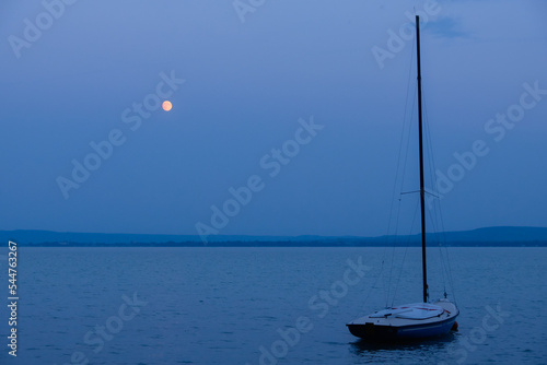 Small sailing boat moored under the moon on Lake Balaton - Revfulop, Hungary photo