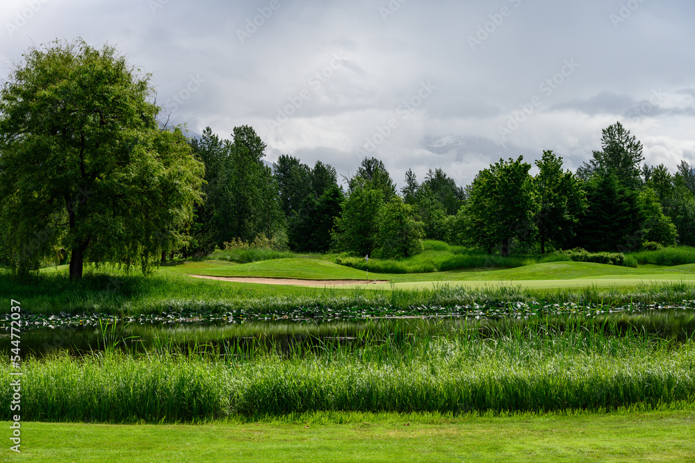 Obraz premium Water hazard and sand trap on a lush green golf course, stormy clouds in background 