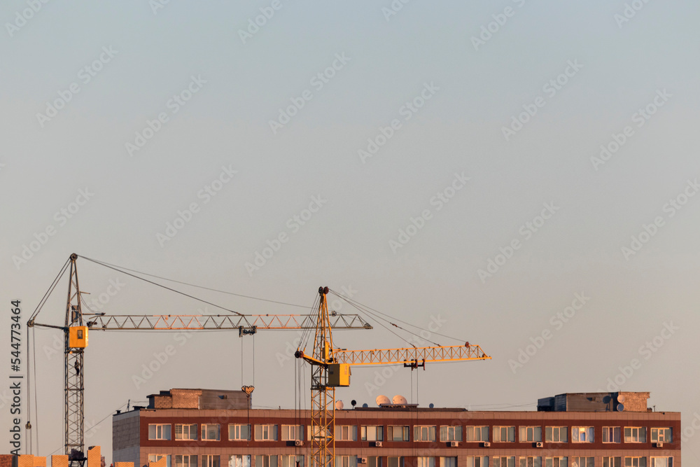 construction cranes over houses in the morning against a clear sky