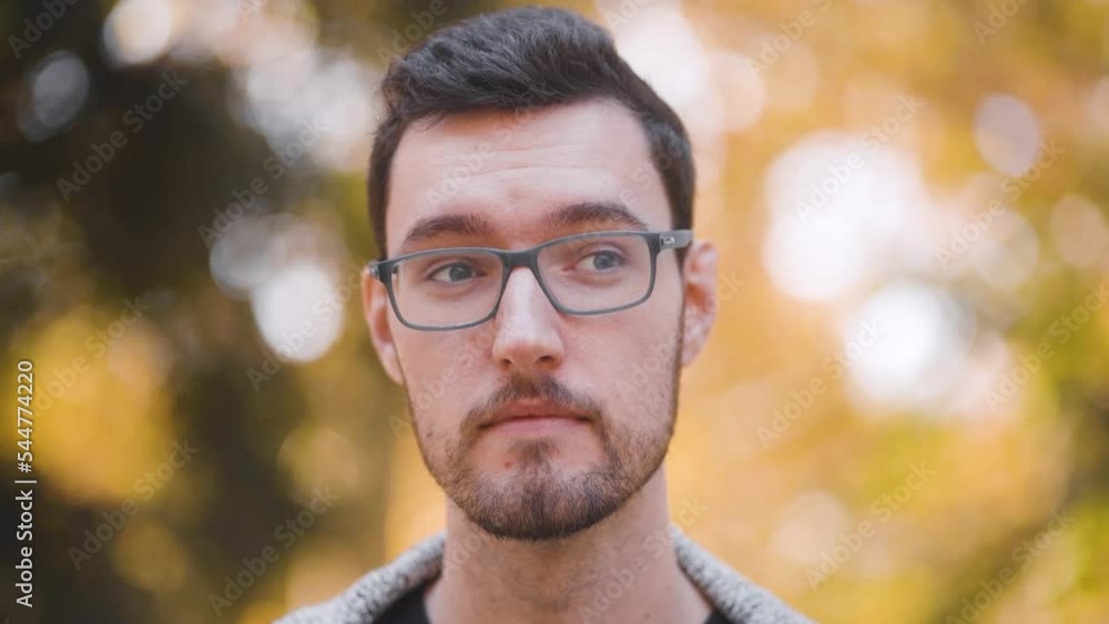 Confused disturbed young man with glasses closeup portrait. human emotion confusion, caucasian man watching distance disapproving in outdoor nature Confused disturbed young man with glasses closeup portrait. human emotion confusion, caucasian man watching distance disapproving in outdoor nature