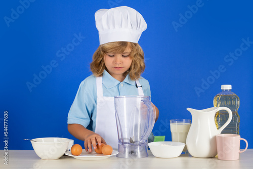 Kid boy in chef hat and apron cooking preparing meal. Little cook with vegetables at kitchen. Natural kids food.