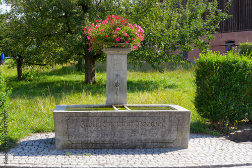 Stone fountain with flower pot on top at rural village of Neerach, Canton Zürich, on a sunny summer afternoon. Photo taken August 26th, 2022, Neerach, Switzerland. photo