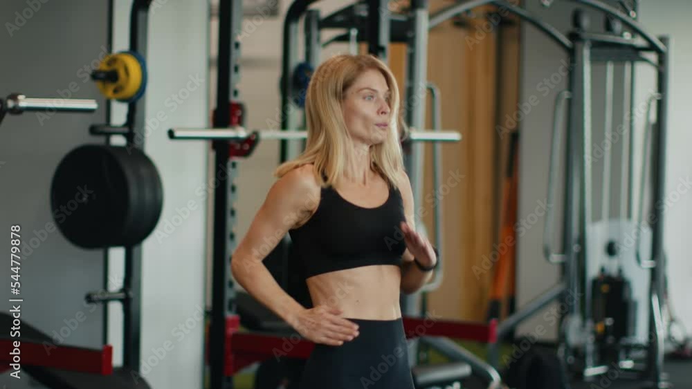 Active middle aged woman running on place and looking at fitness bracelet, checking results of activity and heart rate Active middle aged woman running on place and looking at fitness bracelet, checking results of activity and heart rate