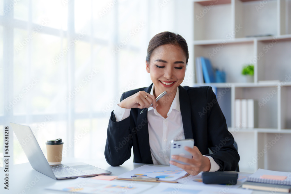 Beautiful Asian businesswoman using smartphone to check tasks, contact clients, respond to chats, transact in the office with a bright and cheerful smile. Beautiful Asian businesswoman using smartphone to check tasks, contact clients, respond to chats, transact in the office with a bright and cheerful smile.