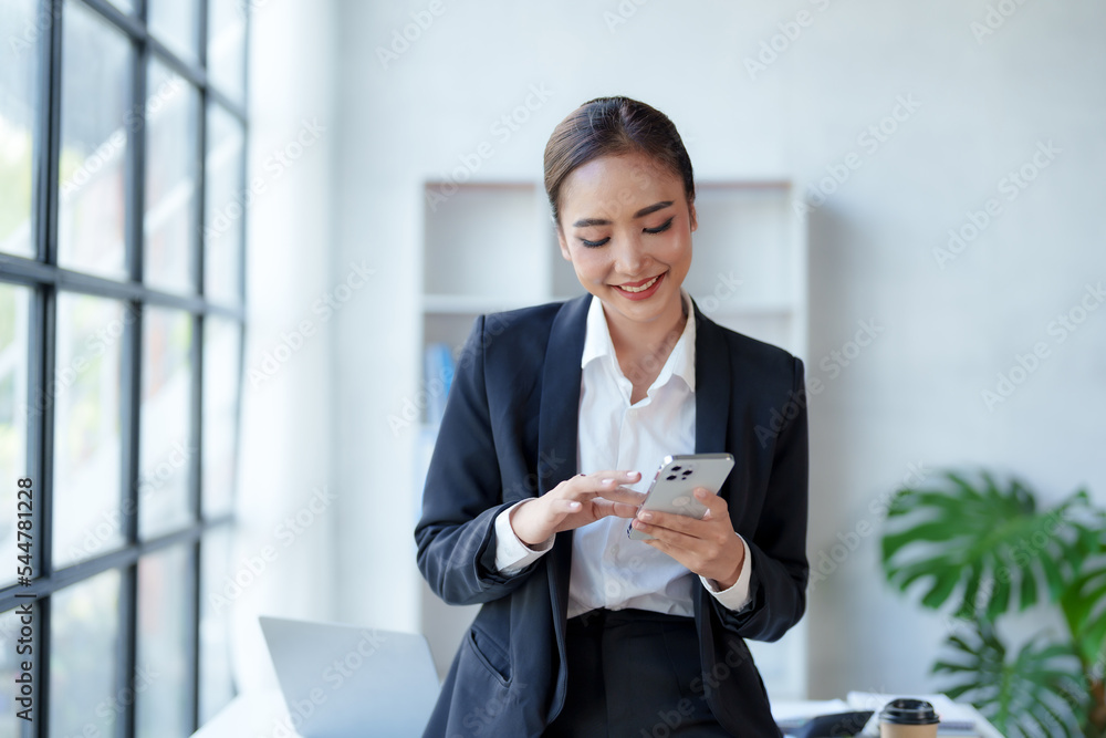 Beautiful Asian businesswoman using smartphone to check tasks, contact clients, respond to chats, transact in the office with a bright and cheerful smile. Beautiful Asian businesswoman using smartphone to check tasks, contact clients, respond to chats, transact in the office with a bright and cheerful smile.