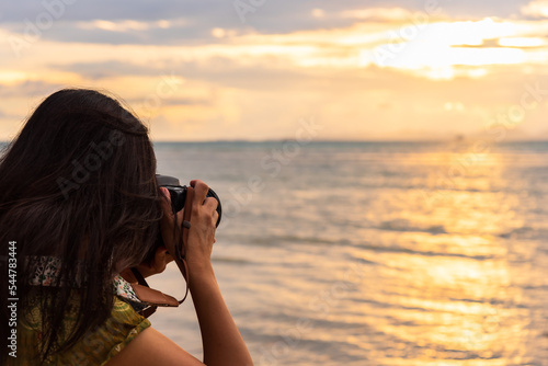 Woman traveler using digital camera to take a photograph of sunset scene at the sea.
