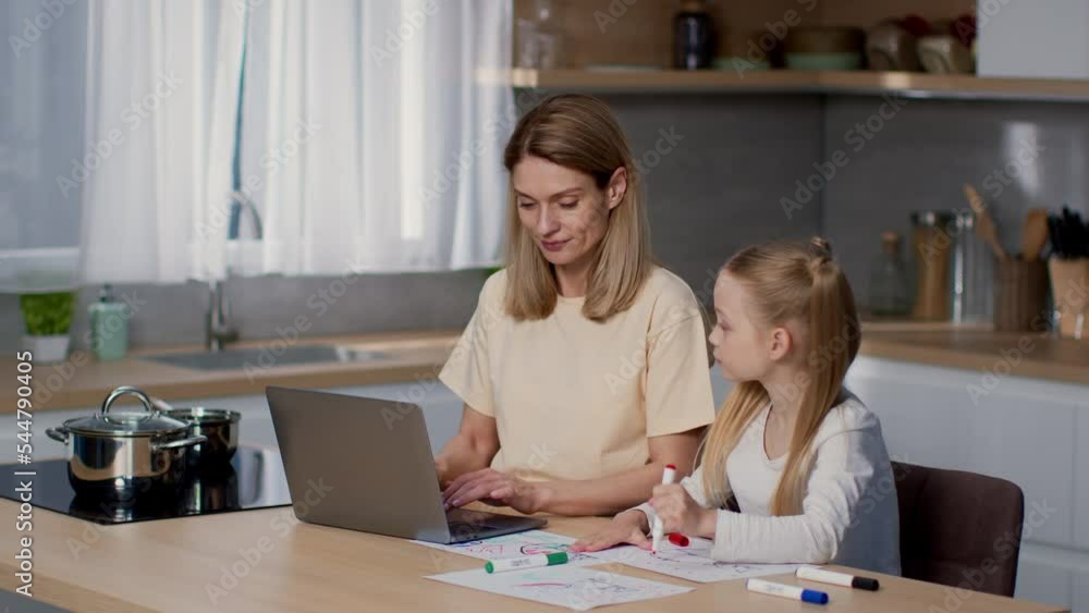 Cozy family evening. Happy little girl drawing picture, her loving mother working on laptop, tracking shot, empty space Cozy family evening. Happy little girl drawing picture, her loving mother working on laptop, tracking shot, empty space