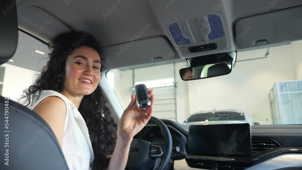 Businesswoman customer satisfied with new purchase and shows car key sitting at steering wheel. Black-haired woman enjoys having new automobile Businesswoman customer satisfied with new purchase and shows car key sitting at steering wheel. Black-haired woman enjoys having new automobile
