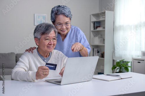 Happy Asian Senior couple at home. Handsome old man and attractive old woman are spending time together. Elderly couple with laptop and credit card in hands. Online shopping © amenic181