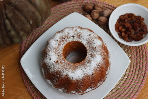 Homemade pumpkin bundt cake with raisins and walnuts on a plate on wooden table