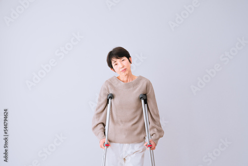 不安そうな表情をする松葉杖をついたミドル女性 医療保険イメージ
