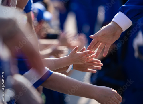 Several Little children giving high fives to their sports heroes outside of a sports arena as they walk by. Close up photo of young boys Touching hands with sports stars