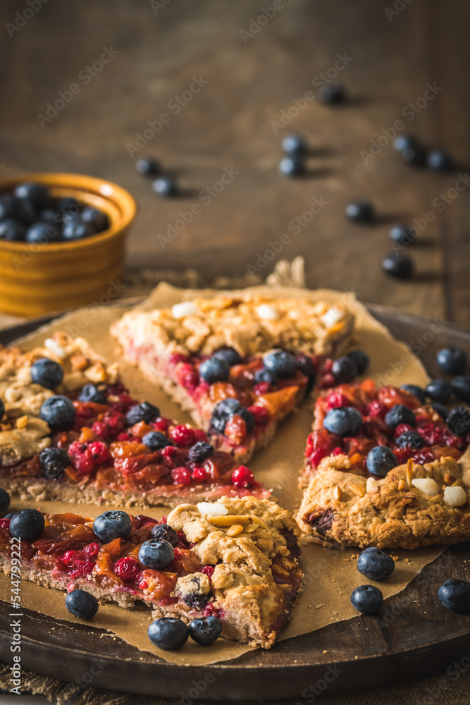 Pieces of a berry galette with fresh blueberries on a rustic wooden table, vertical