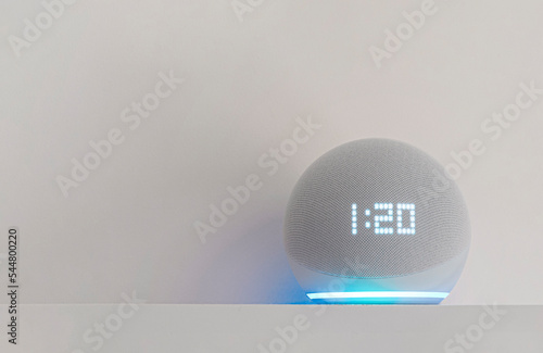 Voice controlled speaker with activated voice recognition on shelf, on wall background.