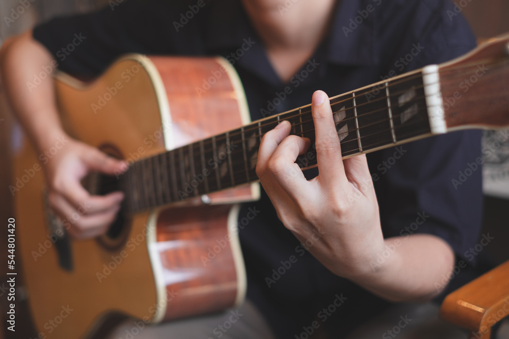 A close up of musician playing an acoustic guitar for entertainment or practicing for perfomance. Concept of indoor activity, lifestyle and leisure. A guitarist is focusing and enjoy playing guitar.