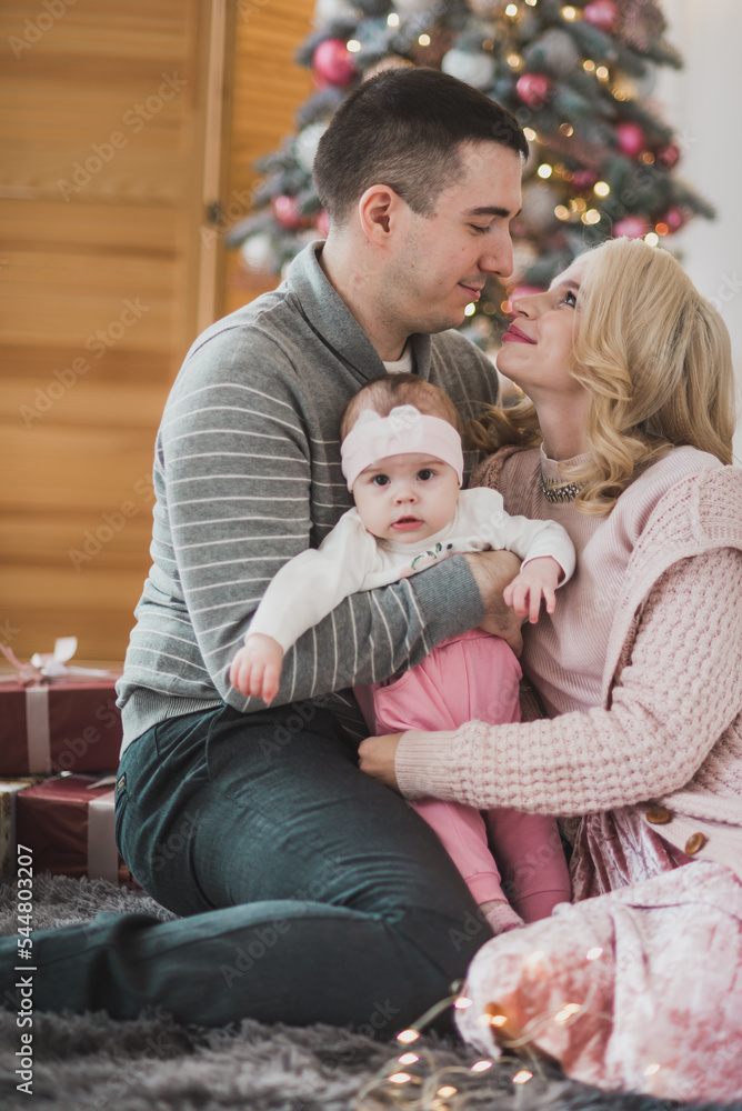 Family mom dad and little baby daughter near a beautiful Christmas tree. Stylish Christmas decorations in pink