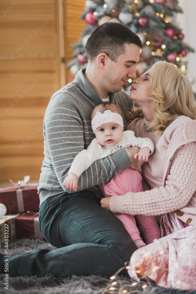 Family mom dad and little baby daughter near a beautiful Christmas tree. Stylish Christmas decorations in pink
