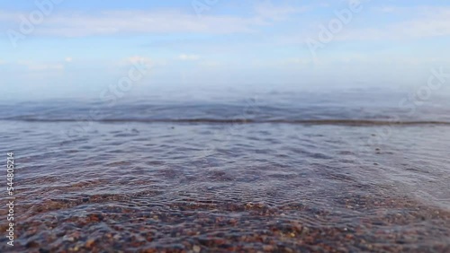 Close-up video. The wave rolls out onto the sandy shore with stones. High-quality shooting in Full HD.