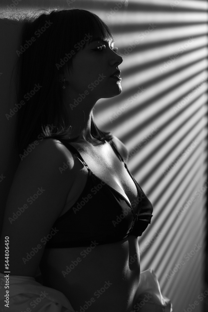 Naklejka premium Portrait of sexy young woman in black sensual lingerie. Girl posing on light wall in studio. Black and white nudity image
