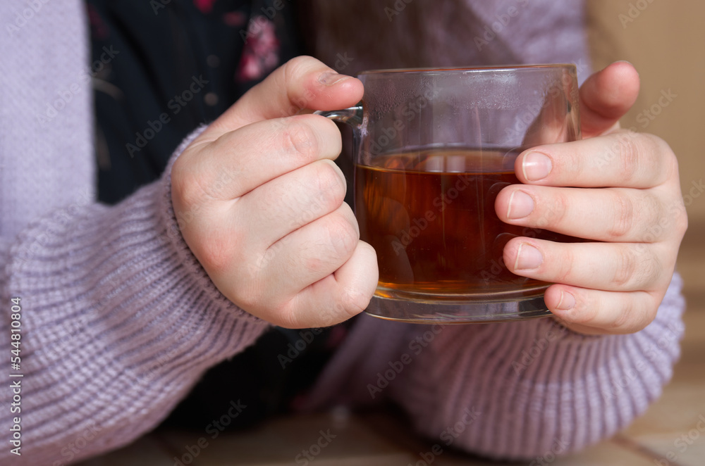Close up of large glass cup with tea in the hands of a woman in a knitted sweater