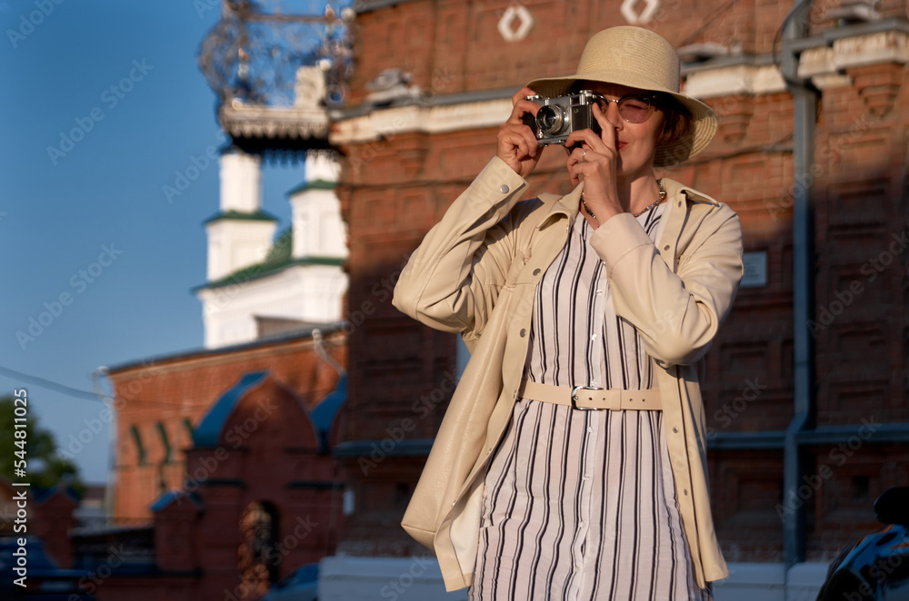Woman tourist in a straw hat takes pictures on the street with a vintage camera Woman tourist in a straw hat takes pictures on the street with a vintage camera