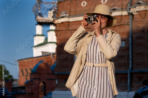 Woman tourist in a straw hat takes pictures on the street with a vintage camera