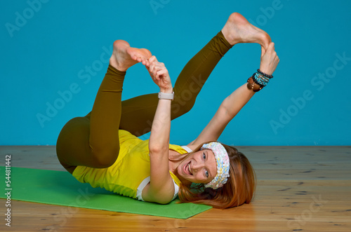 Woman in bright sportswear falls while doing stretching exercise against a blue wall