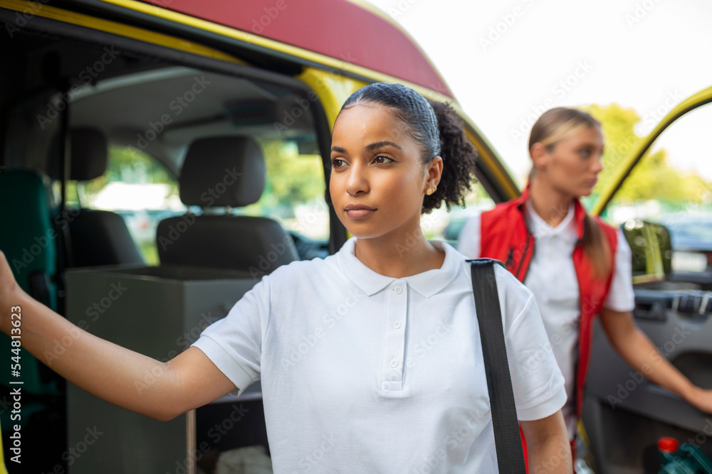 Paramedic nurse and emergency doctor at ambulance with kit. a paramedic, standing at the rear of an ambulance, by the open doors. Paramedic nurse and emergency doctor at ambulance with kit. a paramedic, standing at the rear of an ambulance, by the open doors.