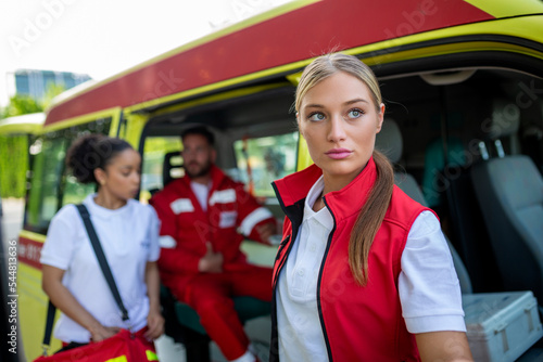 Three multiracial paramedics standing in front of ambulance vehicle, carrying portable equipment © Graphicroyalty