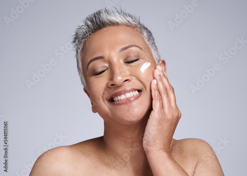 Face, skincare and beauty with a senior woman using cream for antiaging treatment in studio on a gray background. Cosmetics, lotion and cosmetology with a mature female applying cream to skin