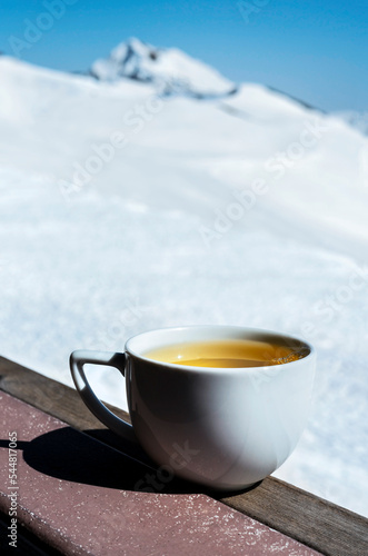 White mug with hot tea on background of snowy mountain range and blue sky Relaxation in nature Landscape natural background copy space