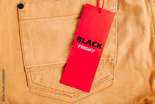 Annual sale Black Friday concept. Red tag with an advertising inscription Black Friday hanging on yellow jeans in a clothing store, close-up