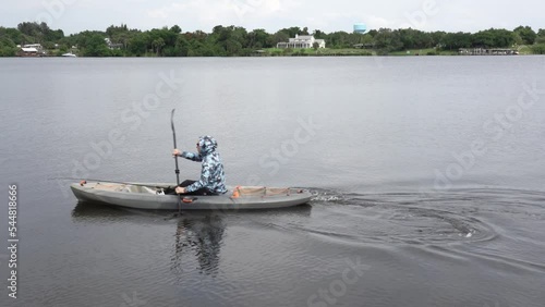 View of a calm river in Florida. A kayak with a fisherman with a fishing rod appears and floats away in the frame