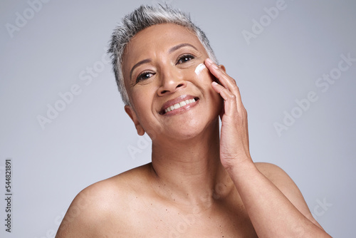 Face, skincare and beauty with a mature woman using moisturizer for antiaging treatment in studio on a gray background. Wellness, facial and portrait with a senior female inside for dermatology care