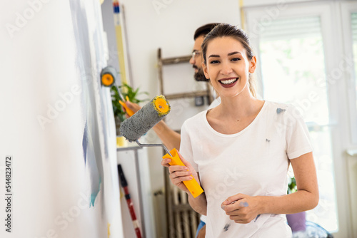 Portrait of smiling young couple painting wall in their home together.