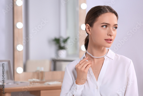 Young woman wearing elegant pearl jewelry indoors  space for text