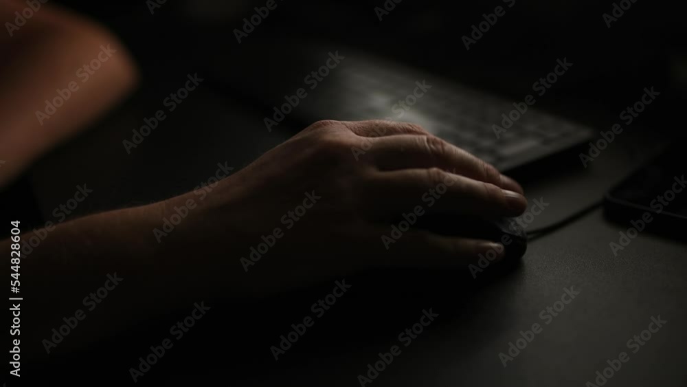 Closeup low key of female hand using computer mouse in dark home office