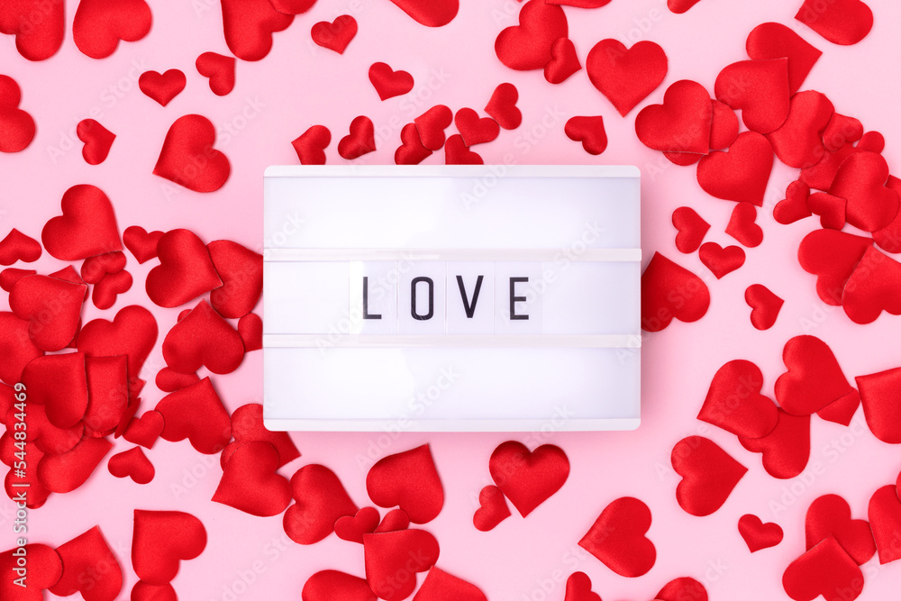Word Love. Lightbox and red textile confetti in a heart shape on a pink background. Word Love. Lightbox and red textile confetti in a heart shape on a pink background.