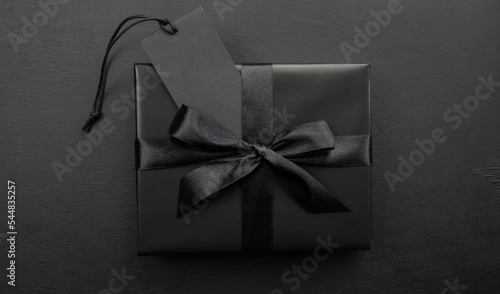 Gift box wrapped in black paper with a black bow on a dark background. Holiday concept. Black Friday. Place for text or advertising.