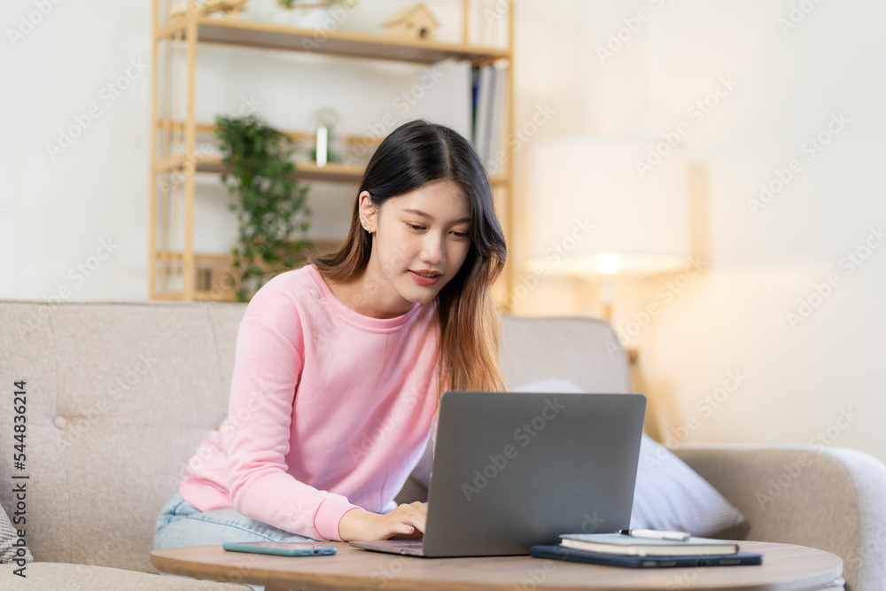 Asian woman smiling and working from home on laptop online to internet on living room sofa. At home with the concept and lifestyle Asian woman smiling and working from home on laptop online to internet on living room sofa. At home with the concept and lifestyle