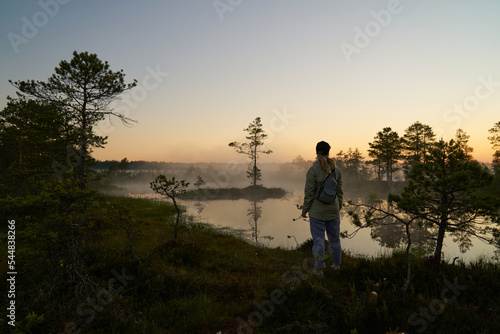 woman tourist meets dawn in nature. Sunset, light and fog, Reflections of trees in lakes . Travel romance. Viru swamps Estonia.