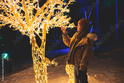 Glowing electric decorations in a winter snowy street, with night decor illumination, Christmas in Europe, with reindeer lamps made of light bulbs and wires, New Year house outdoor yard decoration