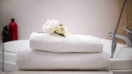 Stacked bath towels and beautiful flowers on table in bathroom