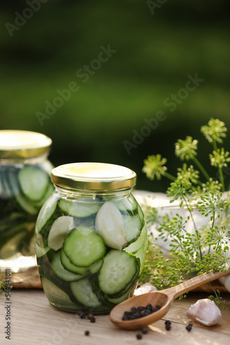 Jars of delicious pickled cucumbers and ingredients on wooden table against blurred background