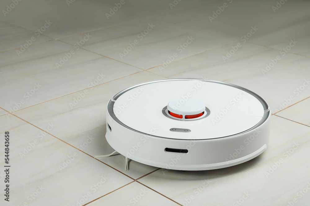 Robotic vacuum cleaner on white tiled floor indoors Robotic vacuum cleaner on white tiled floor indoors