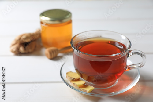 Cup of delicious ginger tea and ingredients on white wooden table, closeup. Space for text