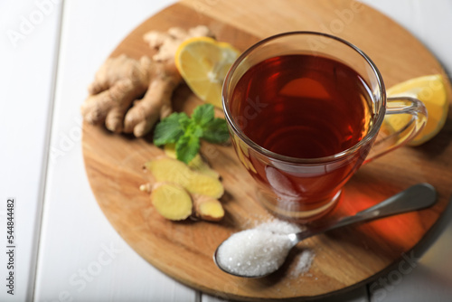 Cup of delicious ginger tea and ingredients on white wooden table, above view. Space for text