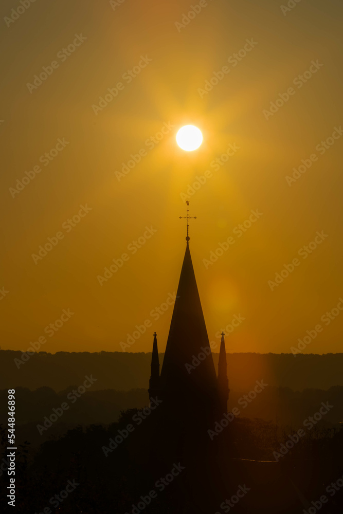 An autumn sunrise in Maastricht with in silhouette the tower of the church of Sint Pieter with the sun aligned above the religious Christian cross