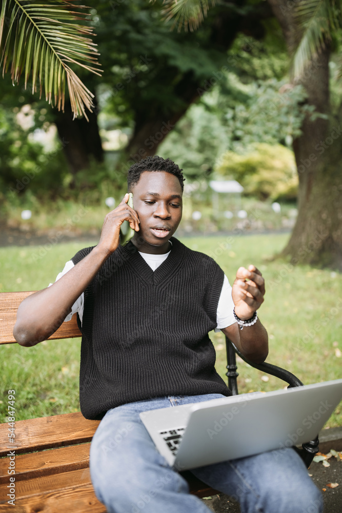 Fototapeta premium Young African man talking on phone disputing over computer, stressed